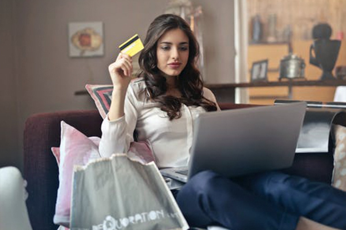 ecommerce Woman sitting on couch with laptop holding credit card to make a purchase