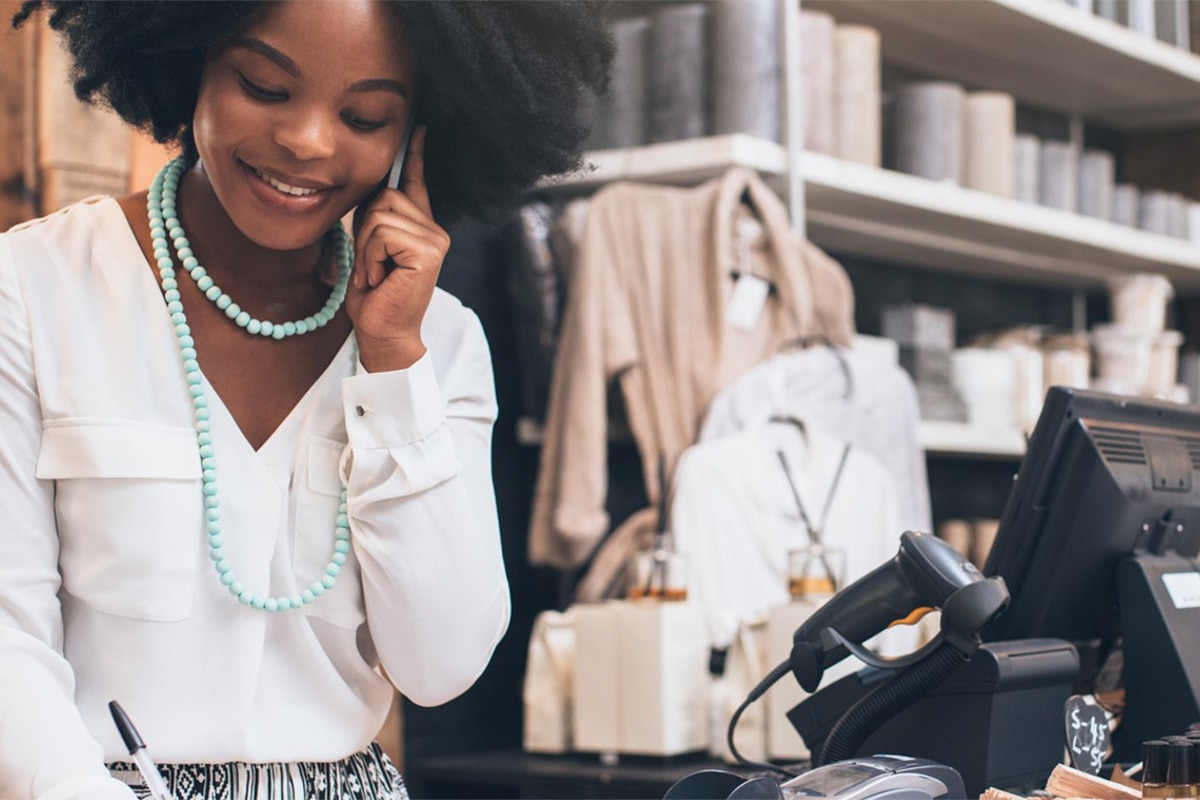 true-human-support Cashier at register smiling while talking on phone and writing something down